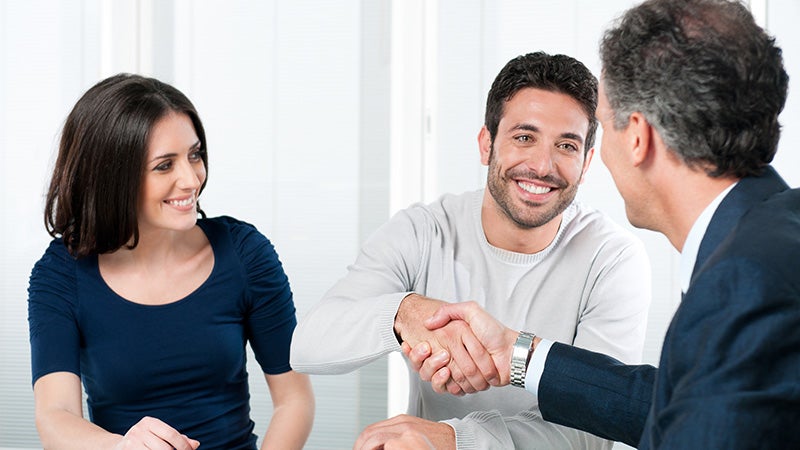 A customer handshake with Salesperson and a his wife watching towards him